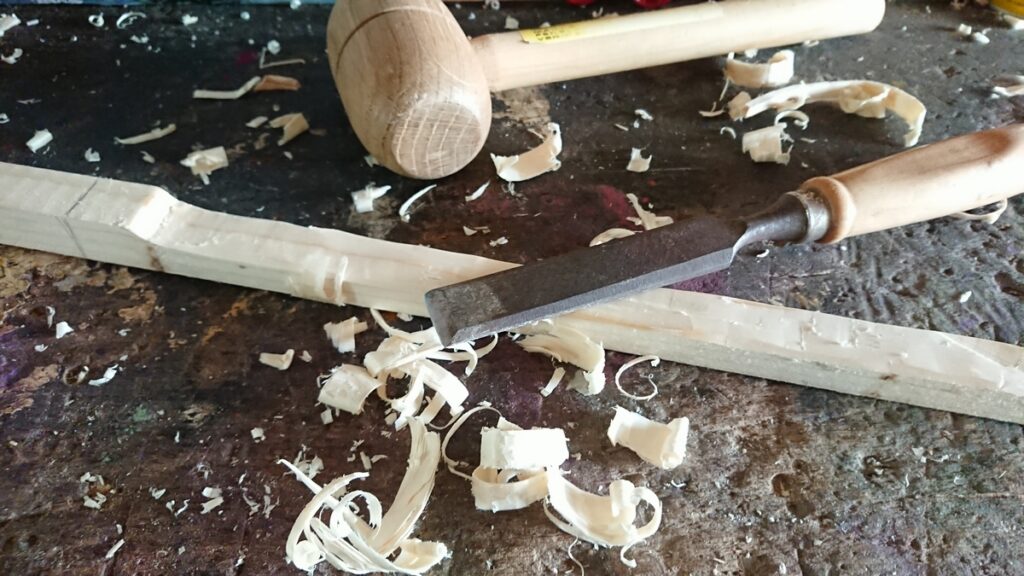 Un tasseau de sapin sur lequel est posé un ciseau à bois.