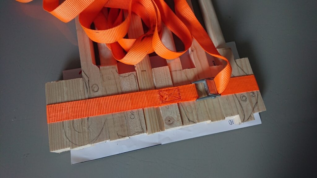 Plusieurs morceaux de tasseaux sont maintenus les uns collés aux autres à l'aide d'une sangle.