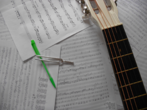 Sur un fond de partition, le manche d'une guitare, un stylo et un diapason.