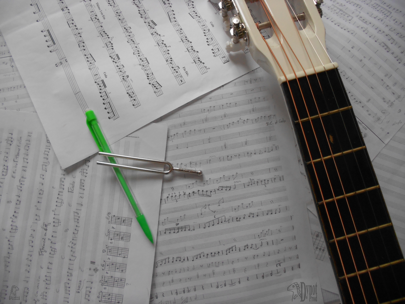 Sur un fond de partition, le manche d'une guitare, un stylo et un diapason.